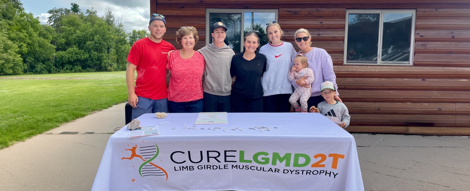 The Cure LGMD 2T team and family gathered behind their table at an outdoor fundraising event